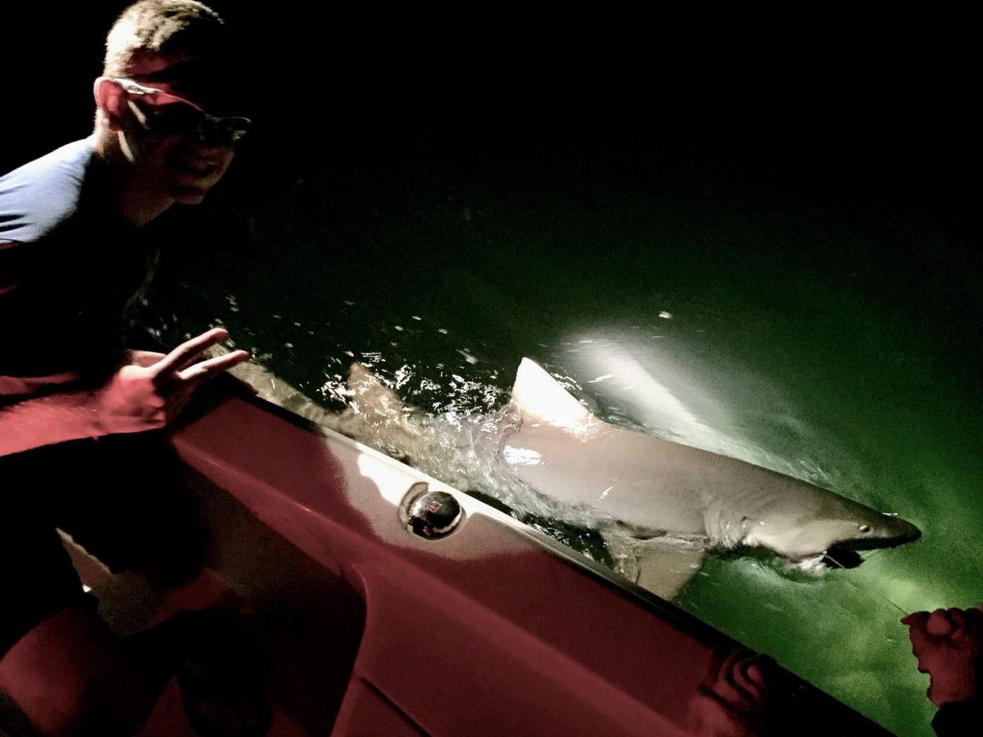 Man giving peace sign next to freshly caught shark