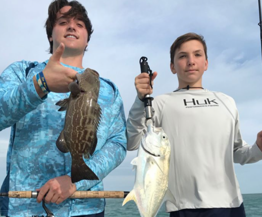 Two young men smiling holding grouper and jack